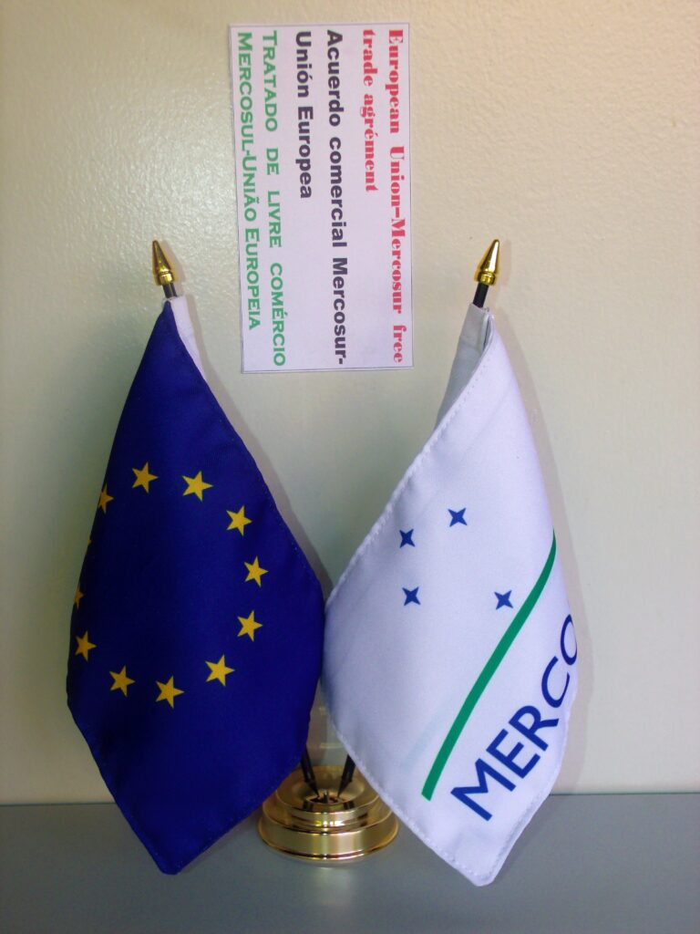 EU and Mercosur officials signing trade agreement with flags in background