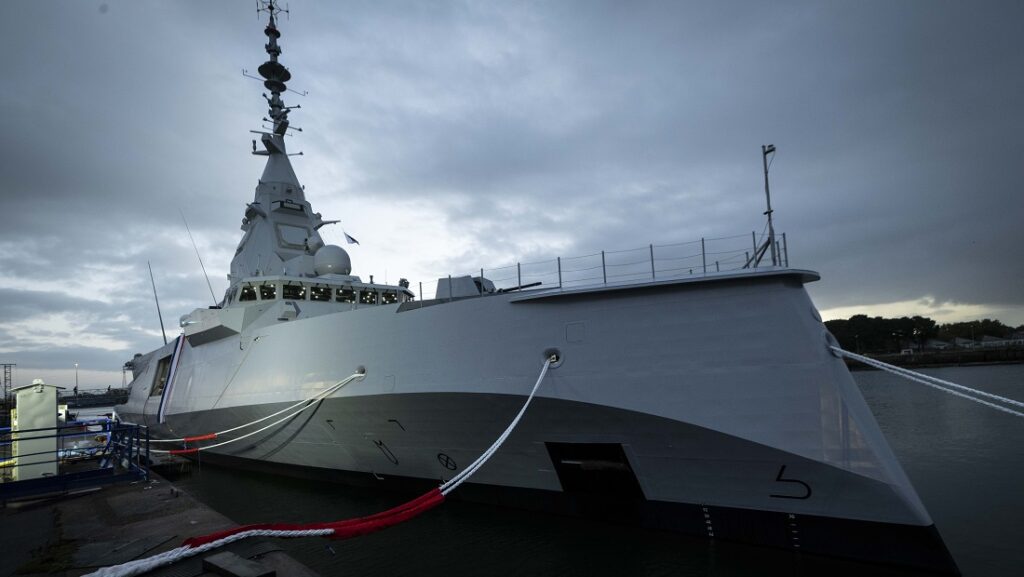Executives handshake at naval shipyard with frigate and submarine background