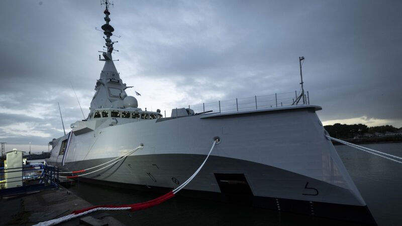 Executives handshake at naval shipyard with frigate and submarine background